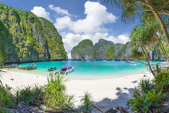 The famous Maya Bay in Thailand's popular Phi Phi Islands with long tail boats in the water and striking white sand
